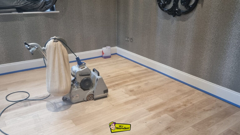 A professional floor sanding machine with a dust bag stands on a taped and partially sanded wooden floor, illustrating a crucial stage in Preparing Your Floor for Sanding.