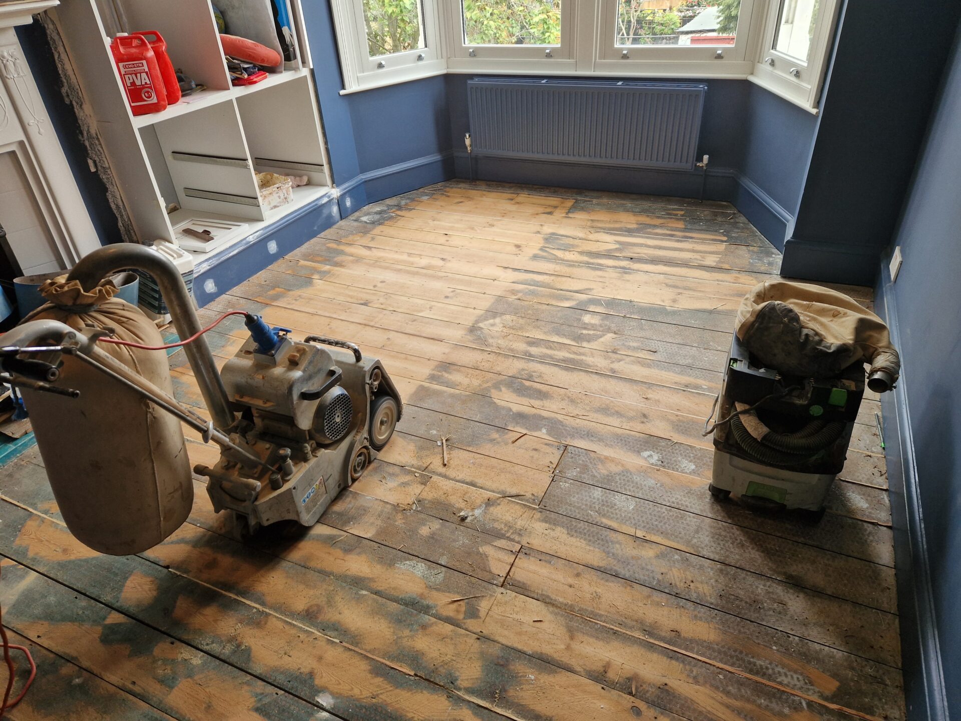 Part-sanded pine floor in a blue living room, with a dustless sanding machine and extractor ready for a Floor Sanding and Matte Finishes renovation.