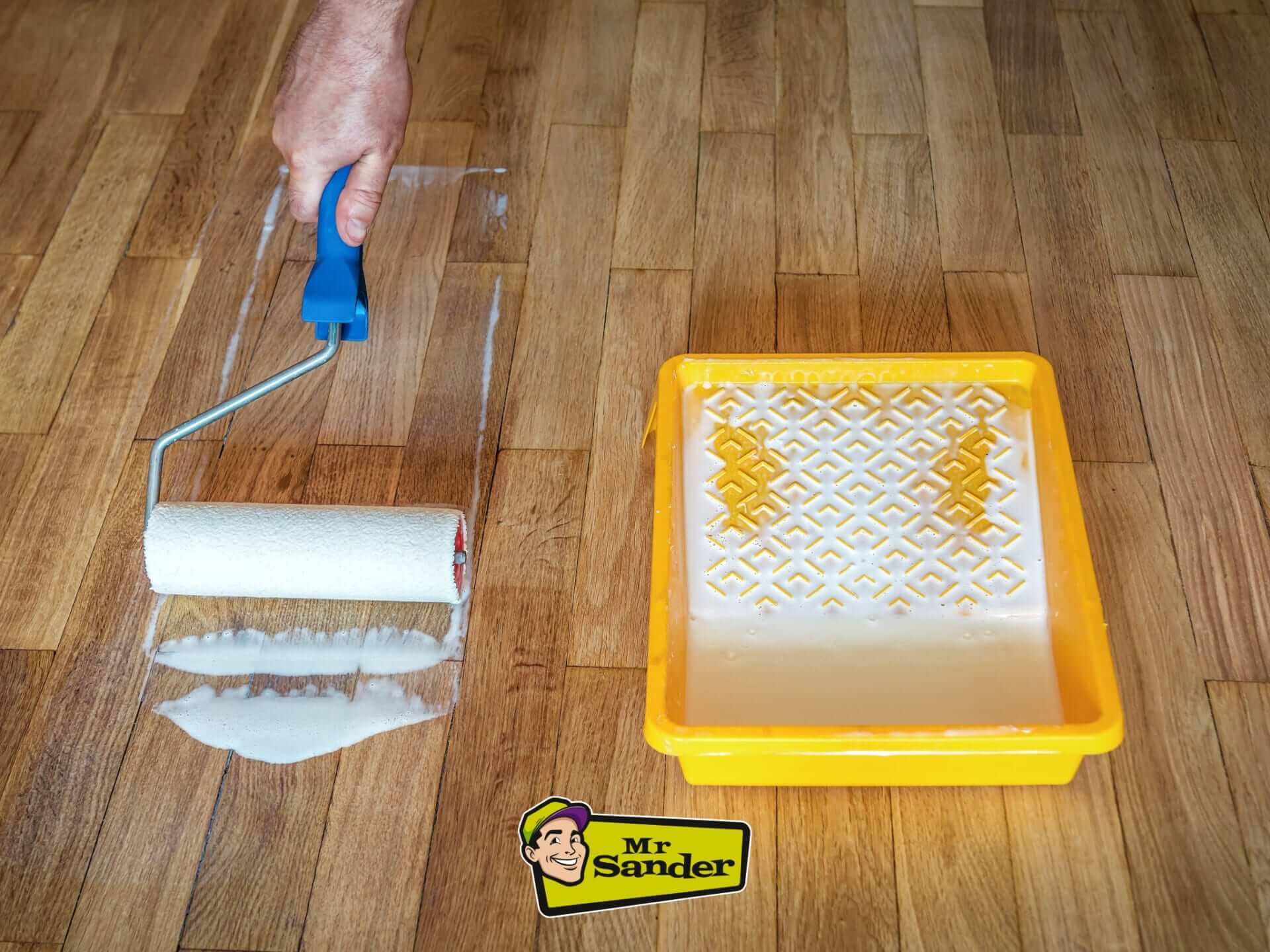 A hand applying a protective finish to a wooden floor using a roller and tray, demonstrating professional floor care by Mr. Sander.