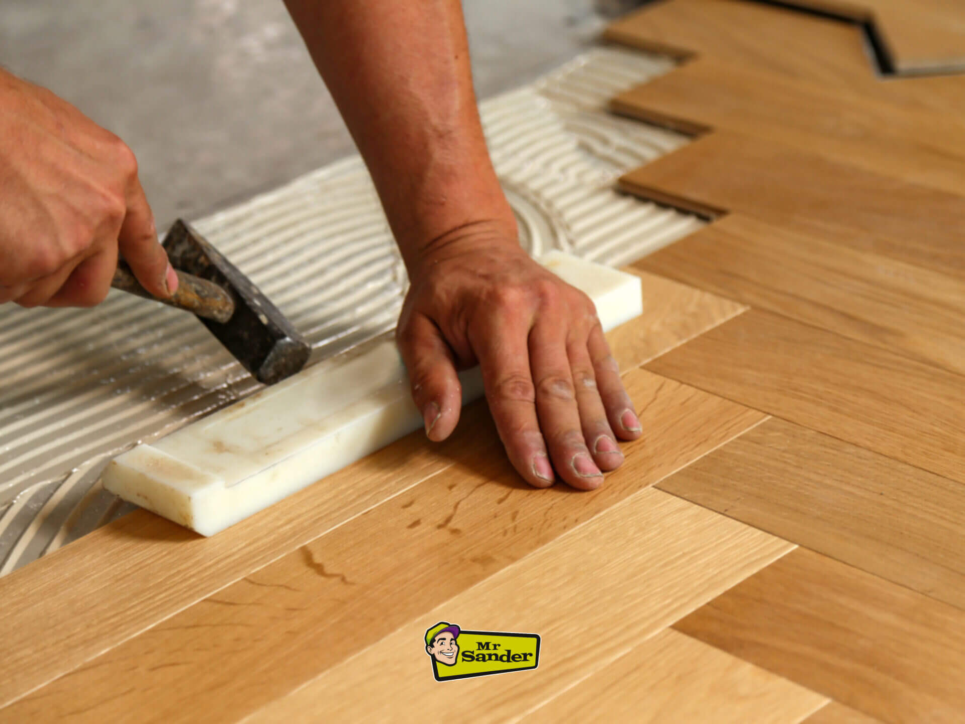 Close-up of a floor fitter precisely aligning herringbone wood parquet boards using adhesive during a West London Floor Fitting project.