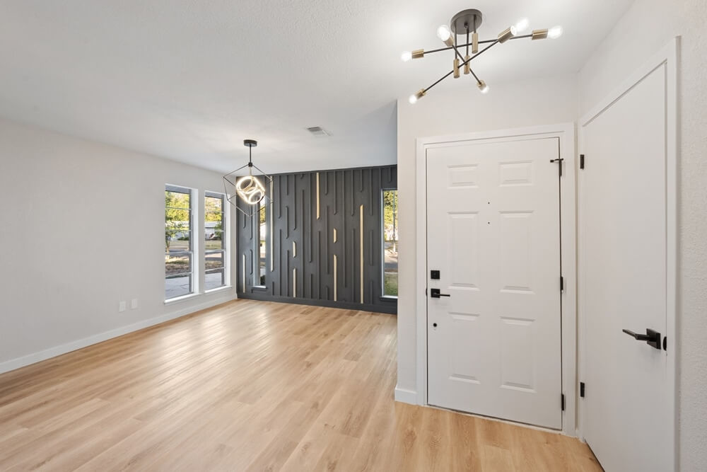 Bright and modern living space with light-colored wooden floors, white walls, and contemporary lighting fixtures. Large windows allow natural light to highlight the freshly sanded and refinished wood flooring. The floor sanding and refinishing were done by Mr Sander®.