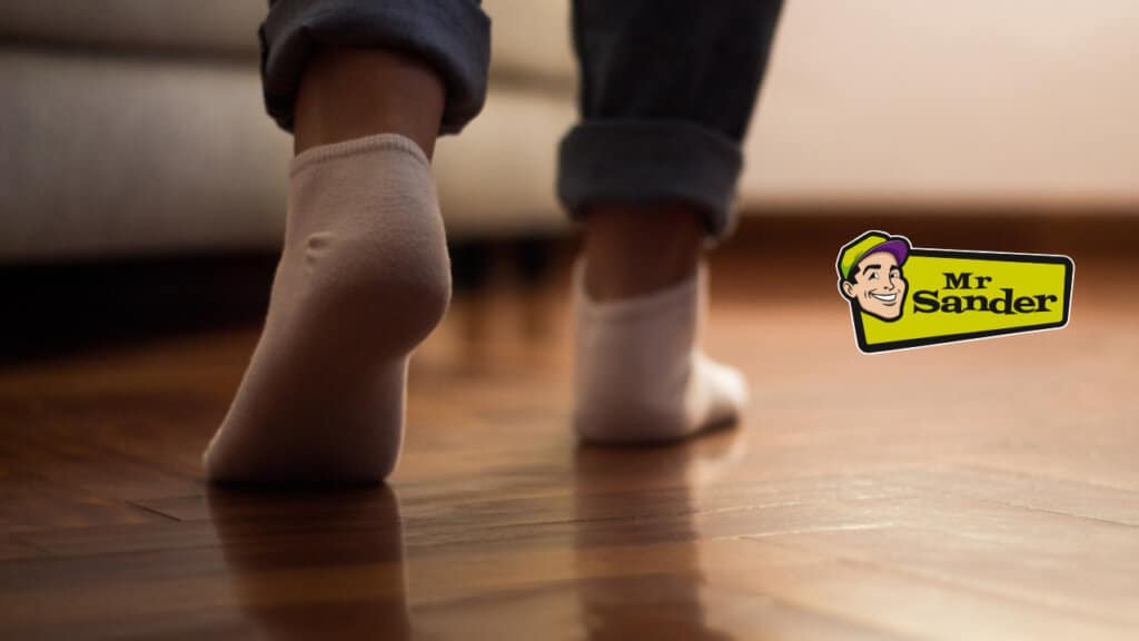 A person wearing socks walks quietly on a polished wooden floor, showcasing its smooth and creak-free finish.