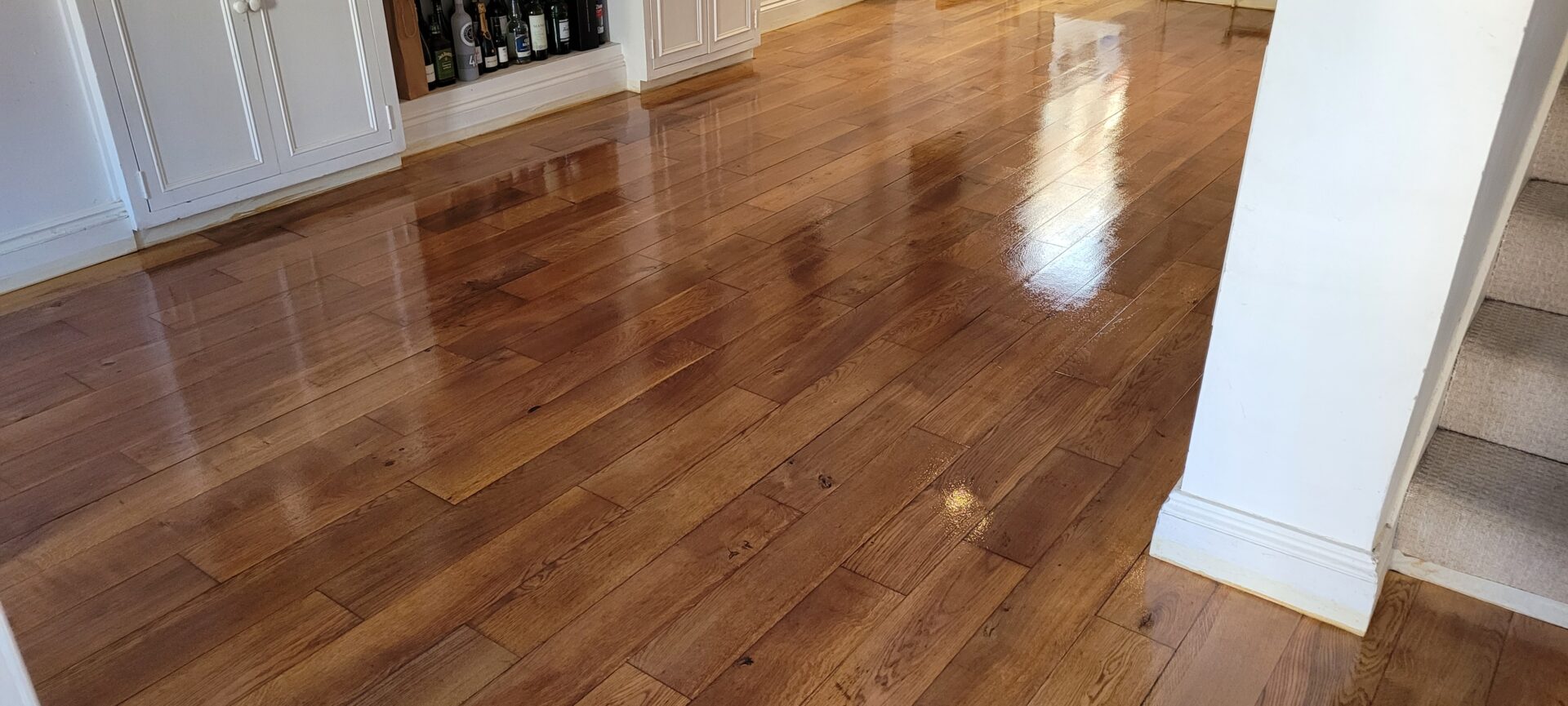 A newly refinished solid oak floor featuring a warm golden satin finish, reflecting a glossy sheen across the living area.