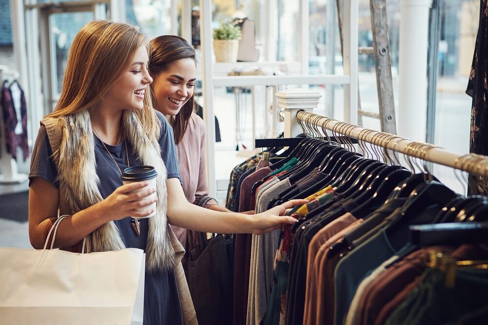 Two young women browsing clothing in a well-lit retail store, illustrating the importance of smooth, polished flooring that can be achieved through Floor Sanding for Commercial Properties.
