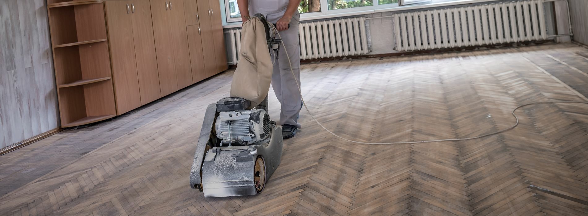 The image showcases the skilled work of Mr Sander® as they undertake the process of sanding hardwood floors. They are utilizing a powerful 250mm x 750mm Bona belt sander, specifically designed for this task. The belt sander is connected to a dust extraction system equipped with a HEPA filter, ensuring a clean and efficient result.