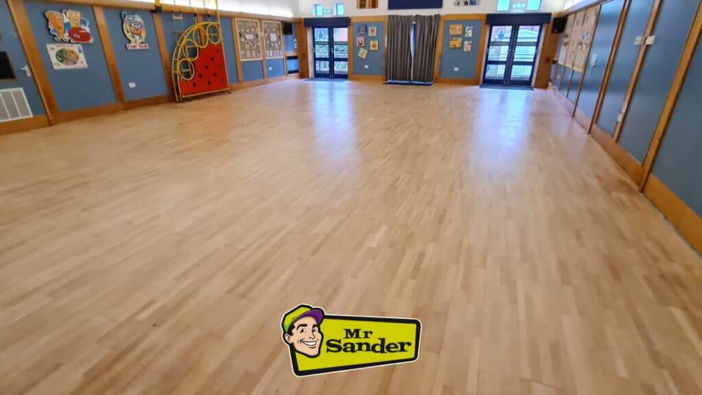 A newly sanded and polished Community floor by Mr. Sander, showing a smooth, reflective wooden surface with surrounding blue and wood-panel walls.
