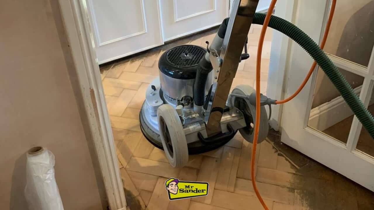 A professional floor sanding machine in action on a herringbone parquet floor during restoration in Shepperton (TW17). The image highlights expert craftsmanship by Mr. Sander.