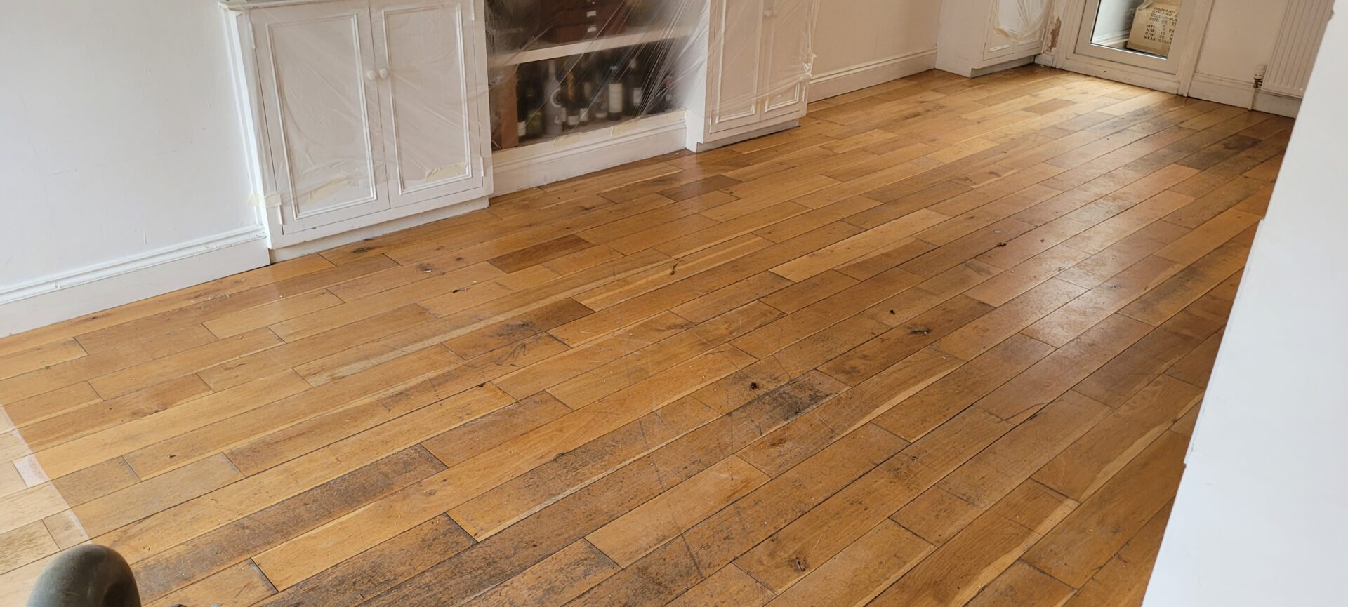 Heavily worn solid oak flooring with a faded golden finish, showing multiple scratches and stains prior to professional floor sanding and repair.