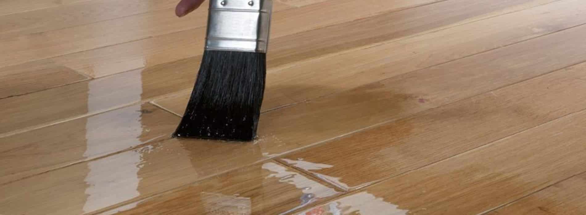 A person holding a paint brush on a hard wood floor.