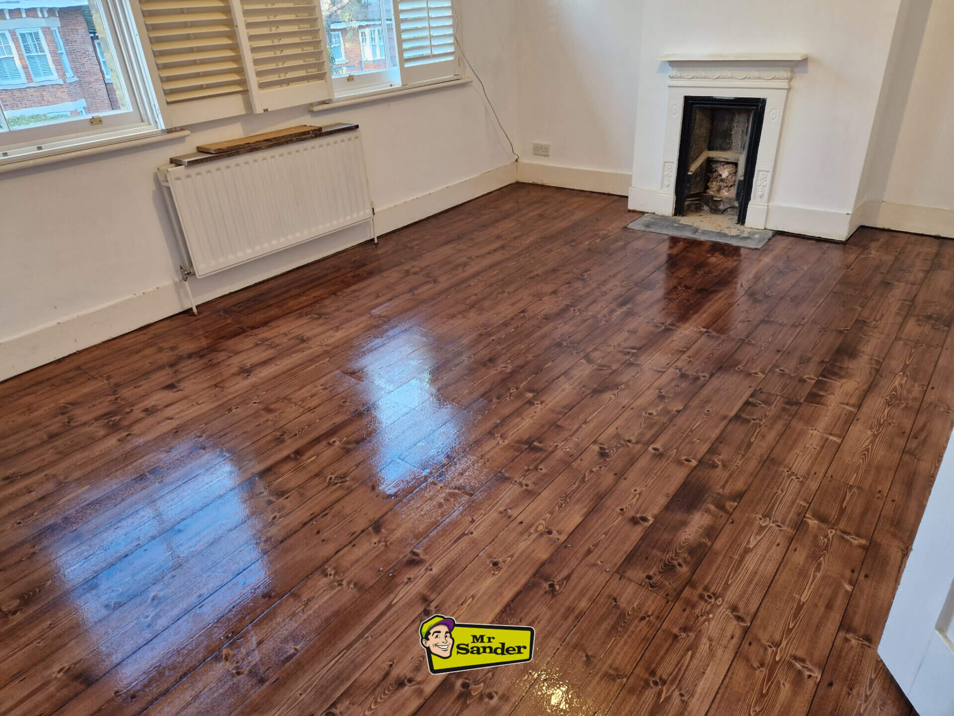Dark, glossy finish on a newly stained pine floor in a living room, highlighting the deep grain and professional sanding result.