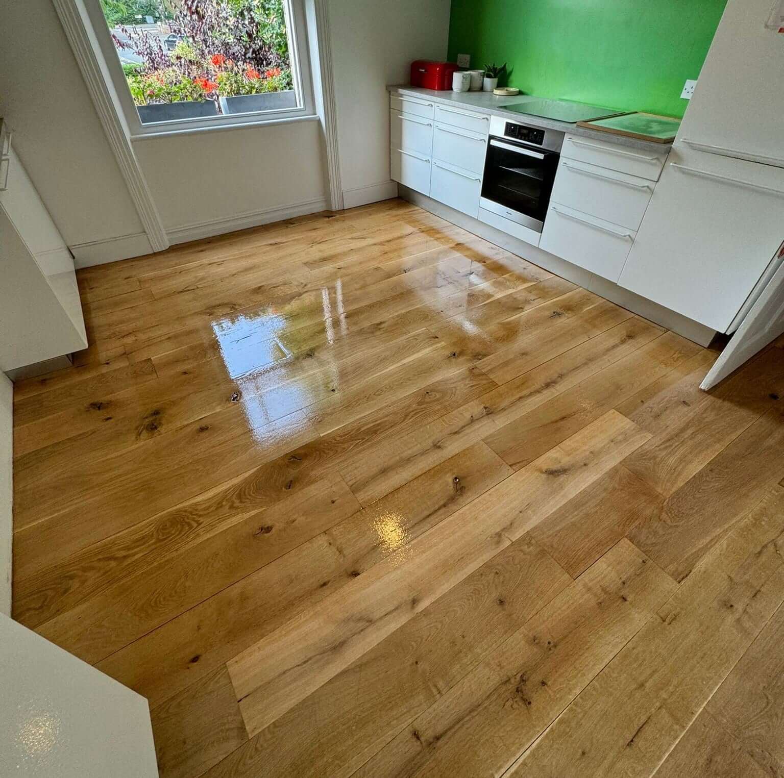 Newly sanded and polished wooden floor in a bright kitchen in Teddington. The floor reflects the natural light streaming through the window, highlighting the fresh and clean finish done by Mr Sander®.