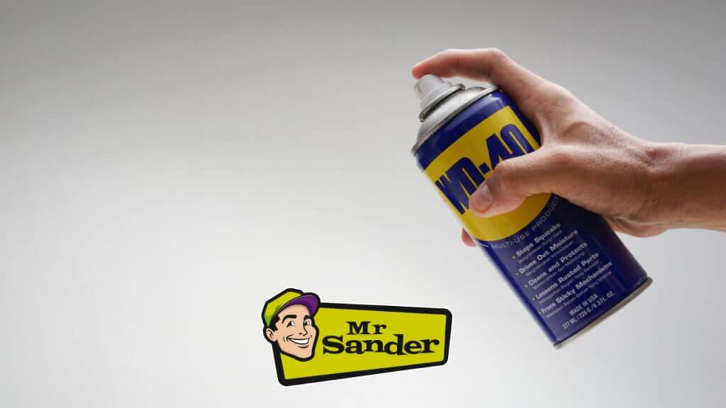 A hand spraying a can of WD-40 against a neutral background with the Mr Sander® logo prominently displayed.