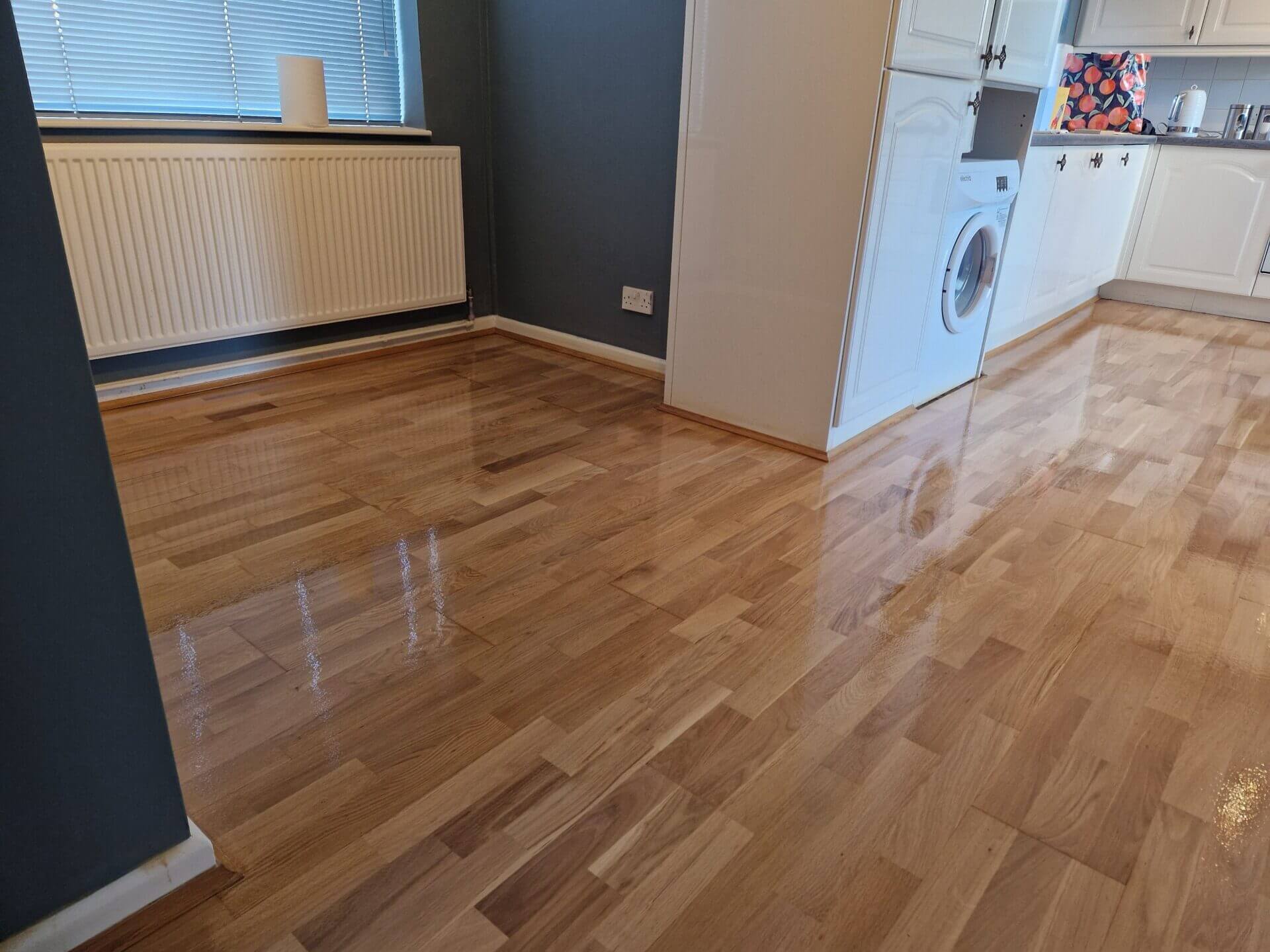 Newly sanded and polished wooden floor in a kitchen area, exemplifying The Art of Floor Sanding with a smooth, reflective finish.
