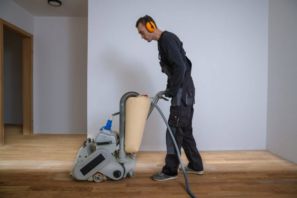 A professional floor sanding technician operating a dustless sanding machine, illustrating The Art of Floor Sanding in a residential setting.
