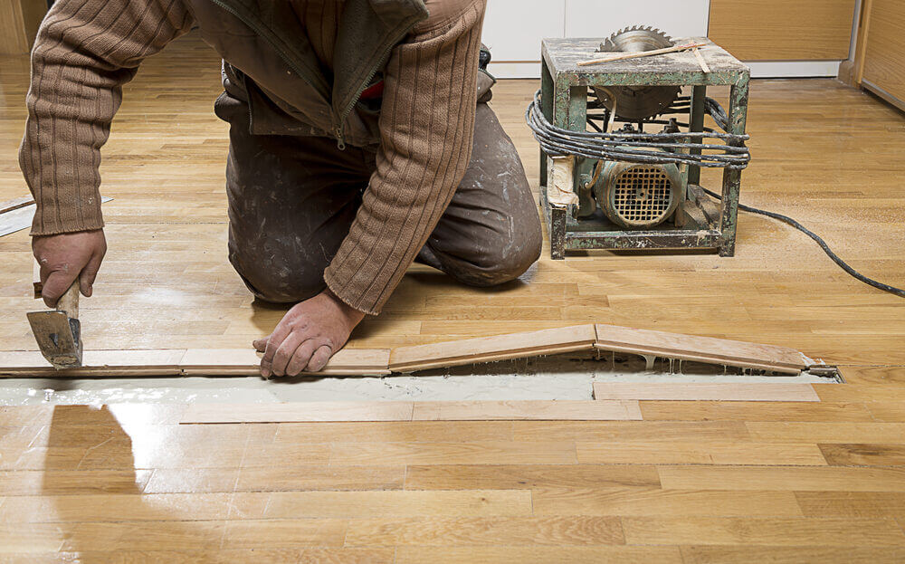 A skilled craftsman repairing hardwood floorboards, highlighting The Art of Floor Sanding’s precision and care.