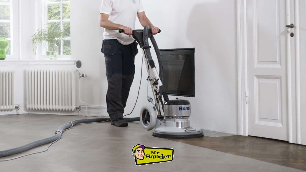 A person using a floor sander machine on a wooden floor.