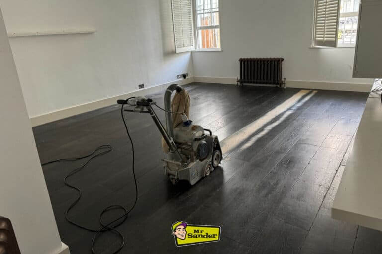 A floor sanding machine in a large, bright room with a dark stained wooden floor, featuring the Mr. Sander® logo.