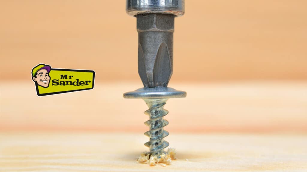 A close-up of a screw being drilled into a wooden floorboard during a floor preparation process by Mr. Sander®.