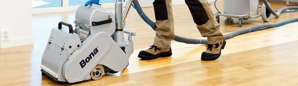 A professional from Mr Sander® is sanding a solid oak hardwood in a living room in Tufnell Park, UK using a Bona Belt sander (AMO110000.3). The machine features a 2.2 kW motor, 230 V voltage, 50 Hz frequency, and a sanding belt size of 200 x 750 mm or 250 x 750 mm. The total weight is 74 kg.