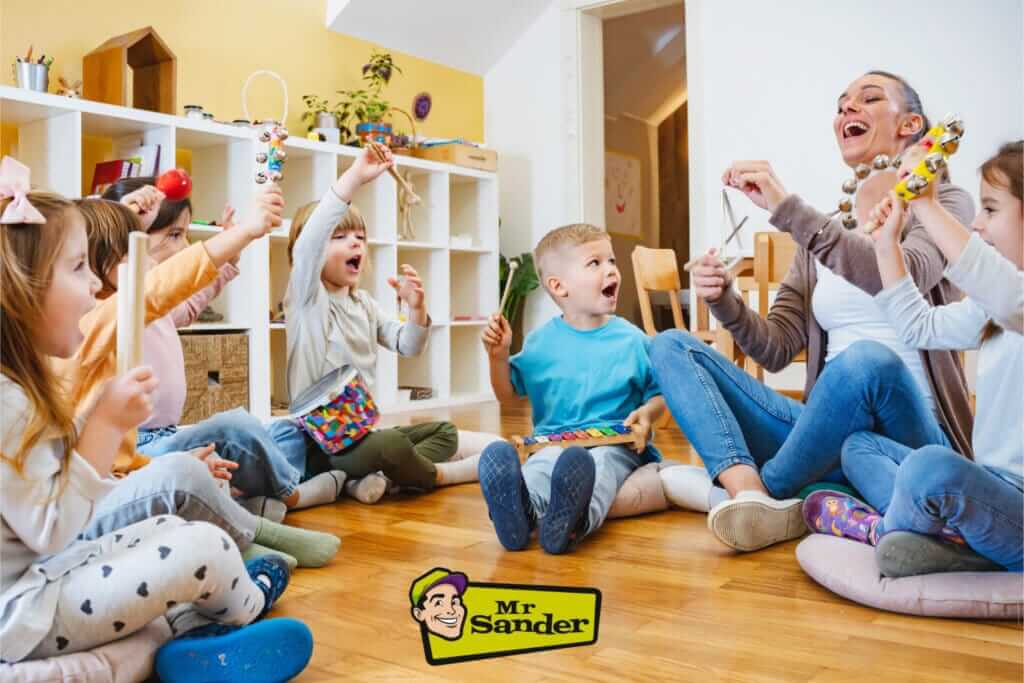 A joyful classroom scene featuring children and a teacher sitting on cushions, playing musical instruments. The bright room has beautifully polished light hardwood flooring, recently sanded and refinished by Mr Sander®. The floor adds a warm and inviting atmosphere to the space, enhancing the overall cheerful environment.