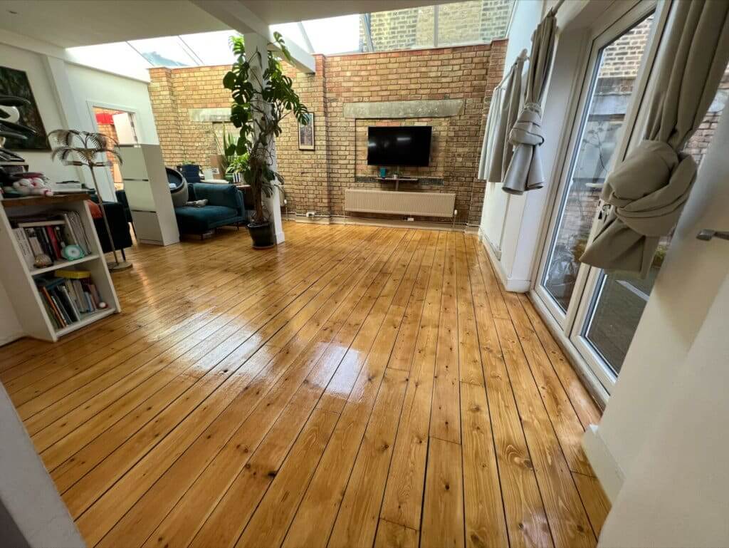 Restored wooden floor in a bright, modern living area with exposed brick walls and large windows, located in Upper Holloway.