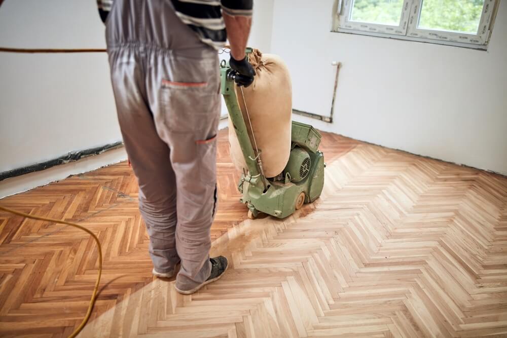 A Mr Sander® technician sanding a parquet floor in a Upper Holloway living room using a LAGLER HUMMEL® machine. Features include powerful LED lighting, high powered aggressive sanding, extremely low dust emissions, quick belt changes, 30+ years lifespan, and easy maintenance. Technical specs: 230 V / 50 CPS / 2.2 kW motor, 200 mm drum width, 2400 rpm drum speed, 200 x 750 mm belt dimensions, 79 kg weight.