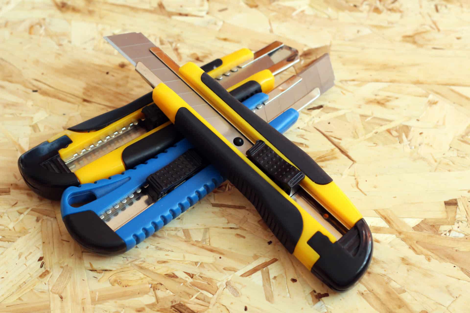 A collection of multi-coloured utility knives with snap-off blades, laid out on a wooden surface.
