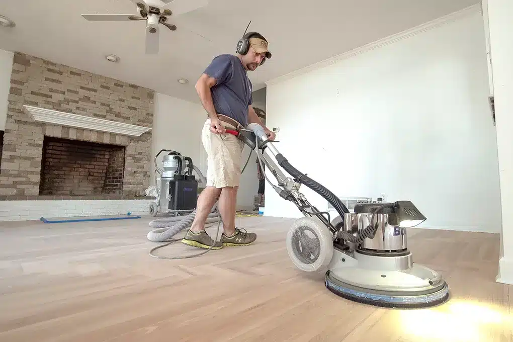 A man operating a Bona floor sander in a living room with a fireplace.