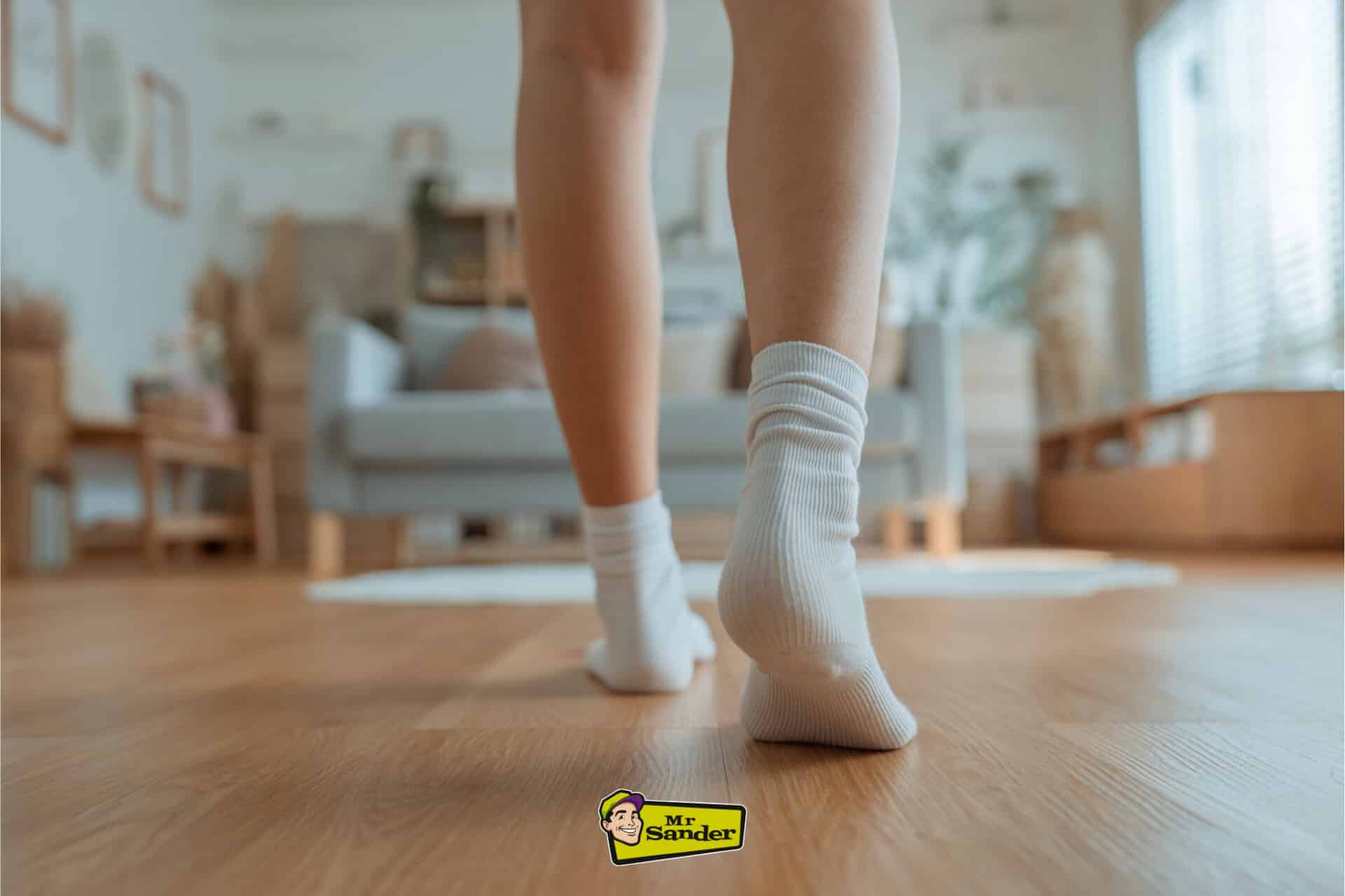 Close-up of a person wearing white socks walking gently on a wooden floor in a cosy living room, illustrating care for freshly sanded floors.