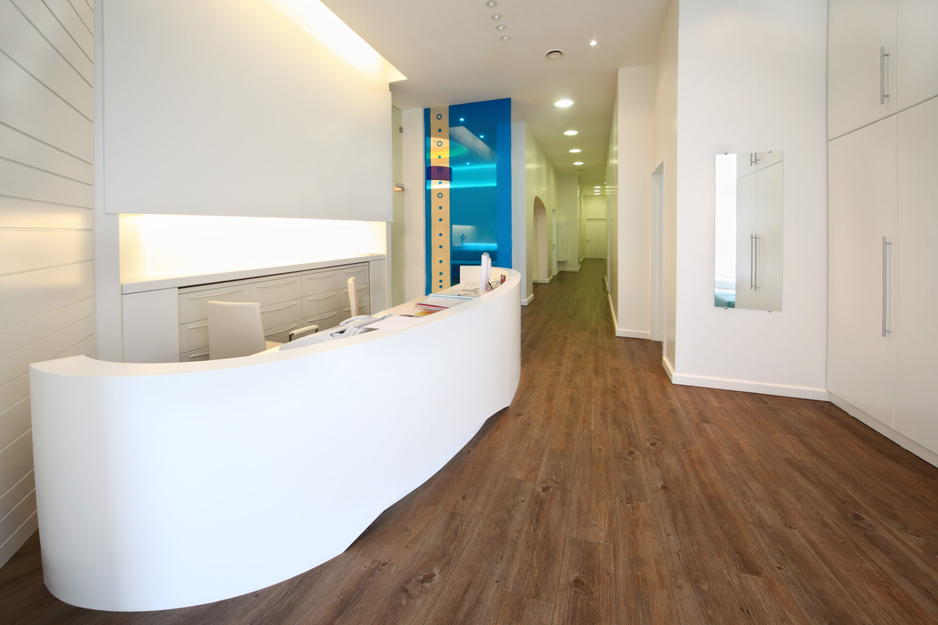 Contemporary clinic reception with curved white desk and walnut-effect luxury vinyl plank flooring after professional Floor Installation for Healthcare Facilities