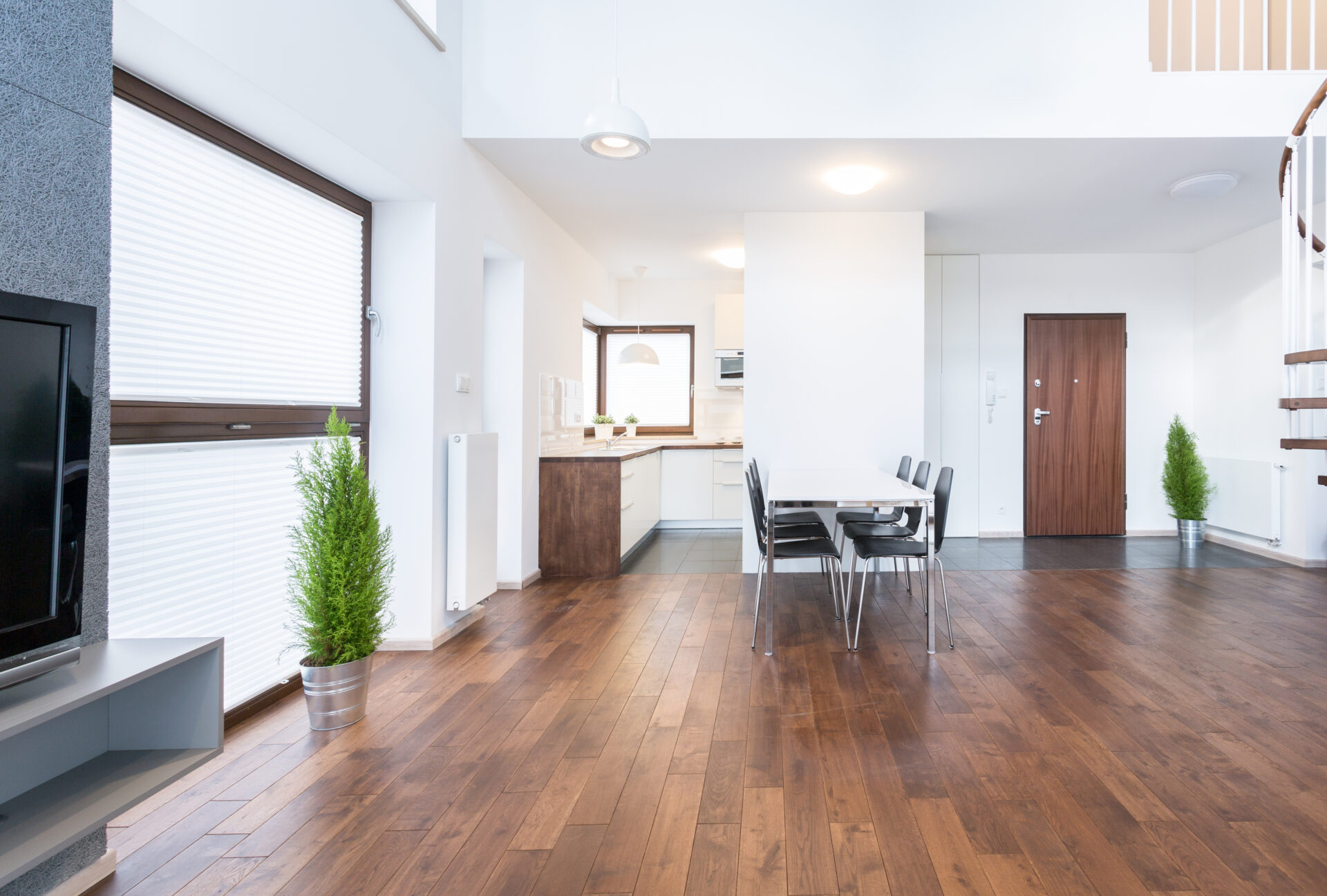 Open-plan loft with warm walnut hardwood floor finished in Colourful Hardwax Oils, contrasting crisp white walls, minimalist dining set and potted evergreens.