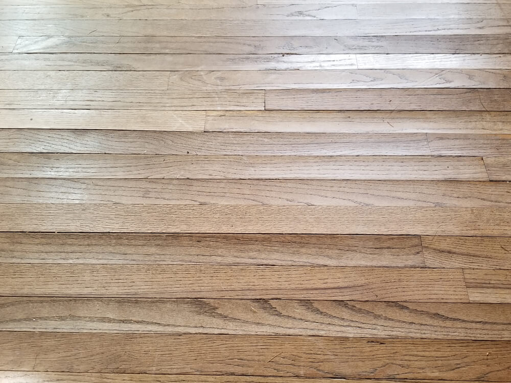 A close-up view of a wooden floor with visible buckling and uneven boards due to skipping the sanding process.