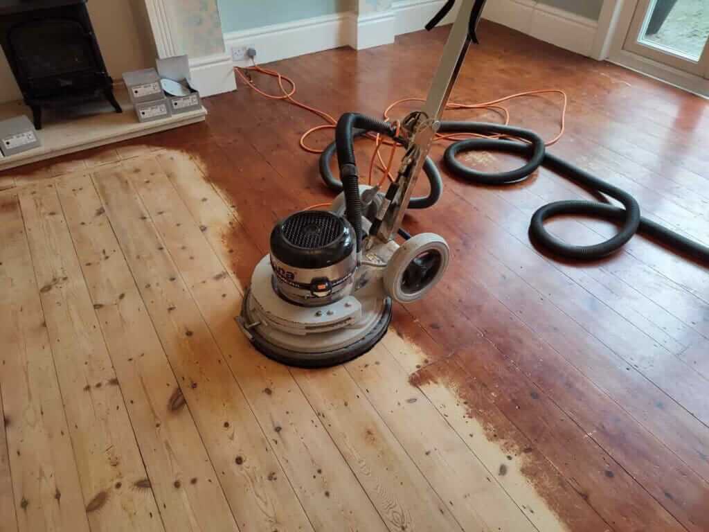 Man from Mr Sander® sanding a pine floor in a living room in, UK, using a Bona FlexiSand 1.9 (AMO310002) buffer. Technical specs: 1.9 kW motor power, 230 V, 50 Hz, 407 mm disc diameter, 147 rpm disc speed, 50 kg total weight, 1170x490x640 mm dimensions, 16 A overload switch.
