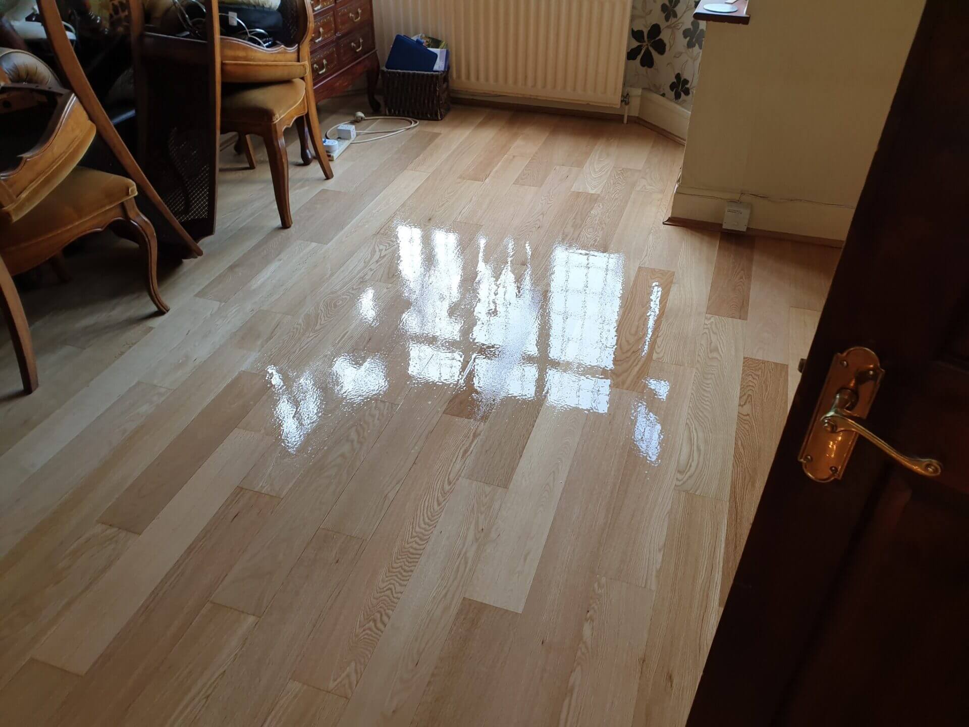 Freshly whitewashed wooden floor with a glossy finish, reflecting natural light in a furnished room.