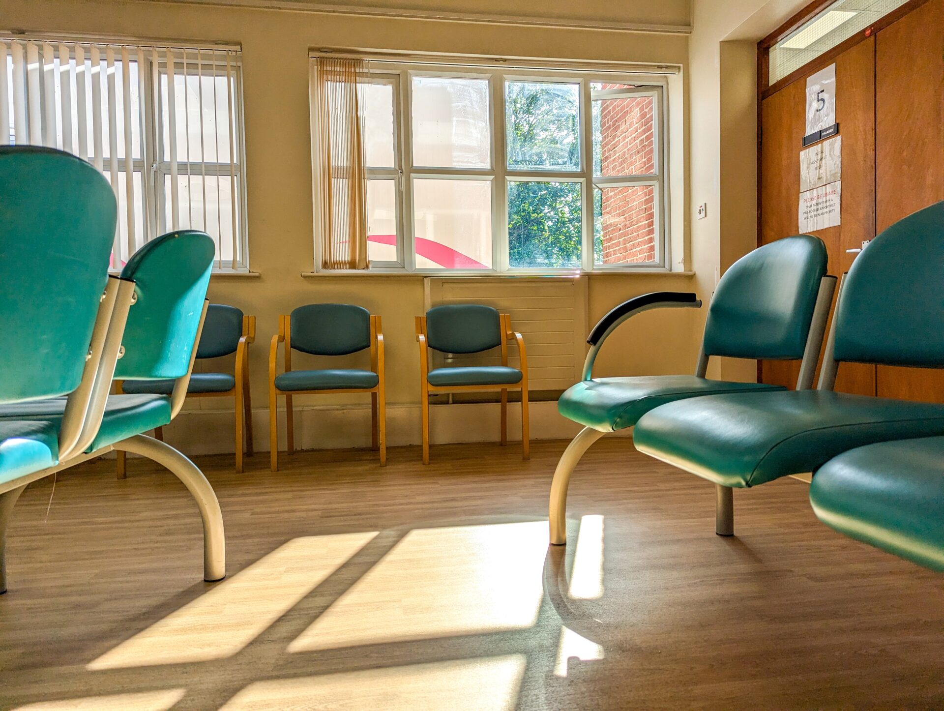 Clinic waiting room with teal chairs, sunlit wood-effect luxury vinyl tile flooring after professional Floor Installation for Healthcare Facilities