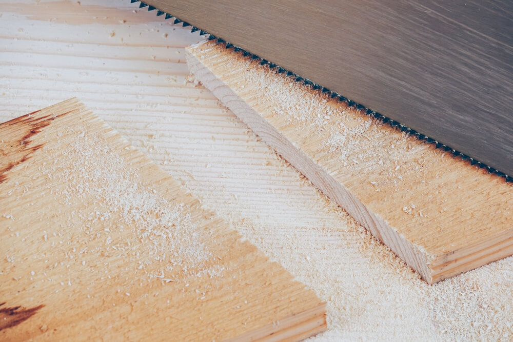 Close-up of a saw cutting wooden planks during a floor-fitting project, leaving sawdust scattered across the boards.