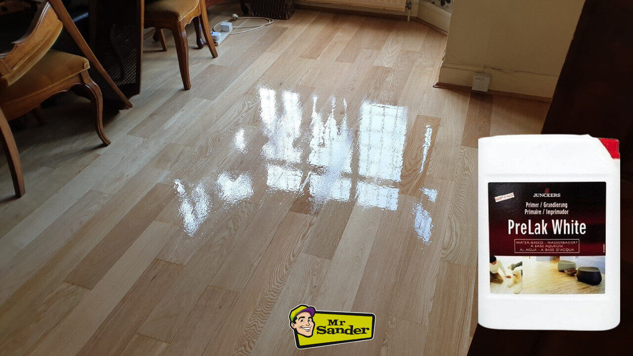 A newly varnished wooden floor with a reflective, glossy surface, shown alongside a container of Junckers Prelak White, illustrating the bright finish achieved through “Wood Floor Finishing with Junckers Prelak White.”