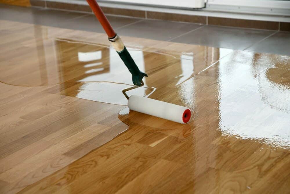 Applying a glossy varnish on a wooden floor with a paint roller.