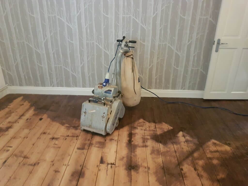 Mr Sander® professional machine is sanding a pine floor in a living room using a Bona Belt sander (AMO110000.3). The machine features a 2.2 kW motor, 230 V voltage, 50 Hz frequency, and a sanding belt size of 200 x 750 mm or 250 x 750 mm. The total weight is 74 kg.