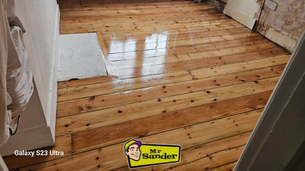 A freshly sanded and refinished pine floor with a warm, honey-colored finish. The floor is clean, shiny, and has a beautiful grain pattern.