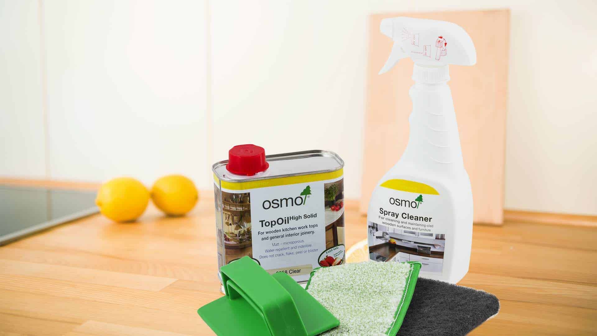 Assorted Osmo cleaning products for wooden worktops displayed with lemons and cleaning pads on a kitchen counter.