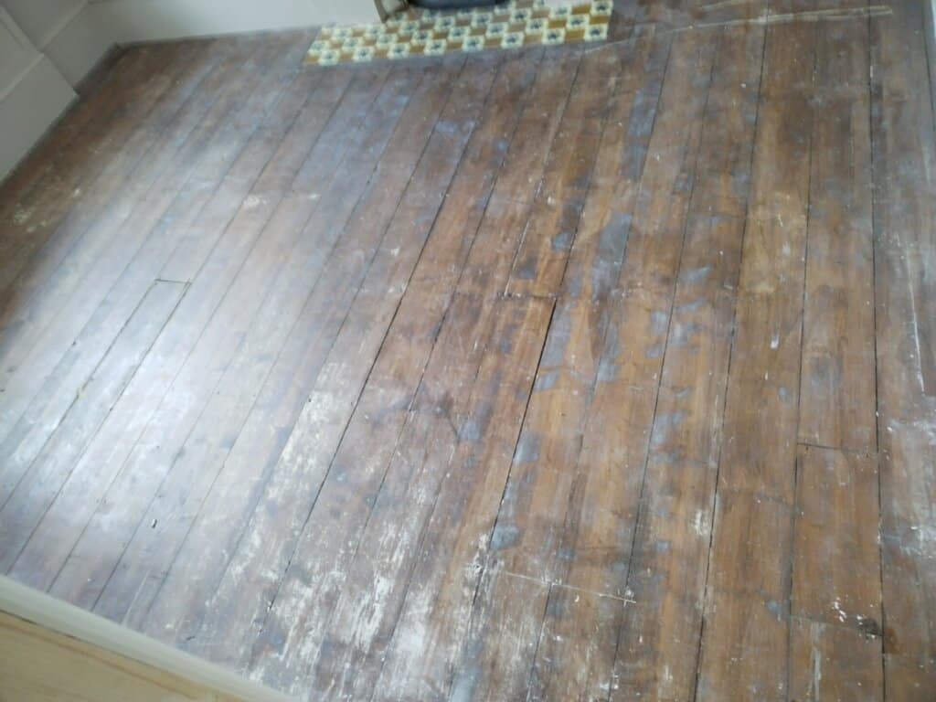 A worn and stained solid wood floor awaiting sanding and refinishing, featuring visible imperfections and aged patina.