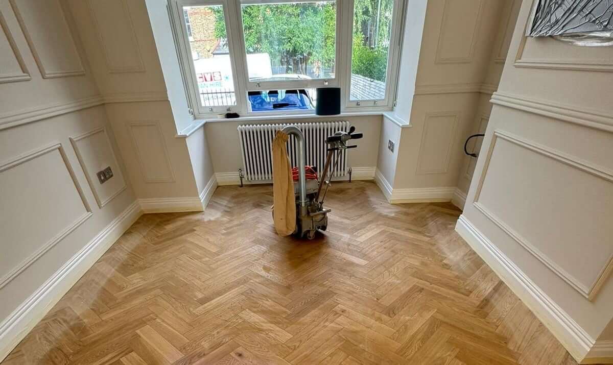 Man from Mr Sander® sanding parquet floor in a living room in Biggin Hill, UK, using Bona Belt sander (AMO110000.3), 2.2 kW motor power, 230 V, 50 Hz, 250x750 mm size, 200 & 250 mm drum width, sanding belt size 200x750 mm or 250x750 mm, total weight 74 kg, for precise and efficient sanding.