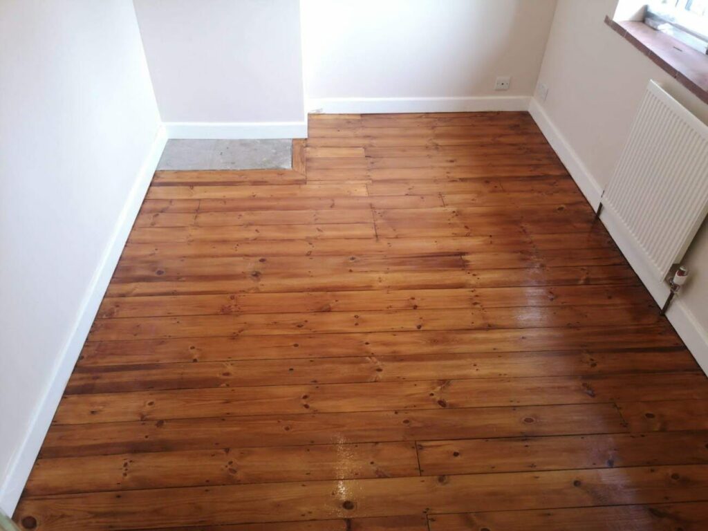 Refinished pine wood flooring in a well-lit empty room with white walls and a radiator.