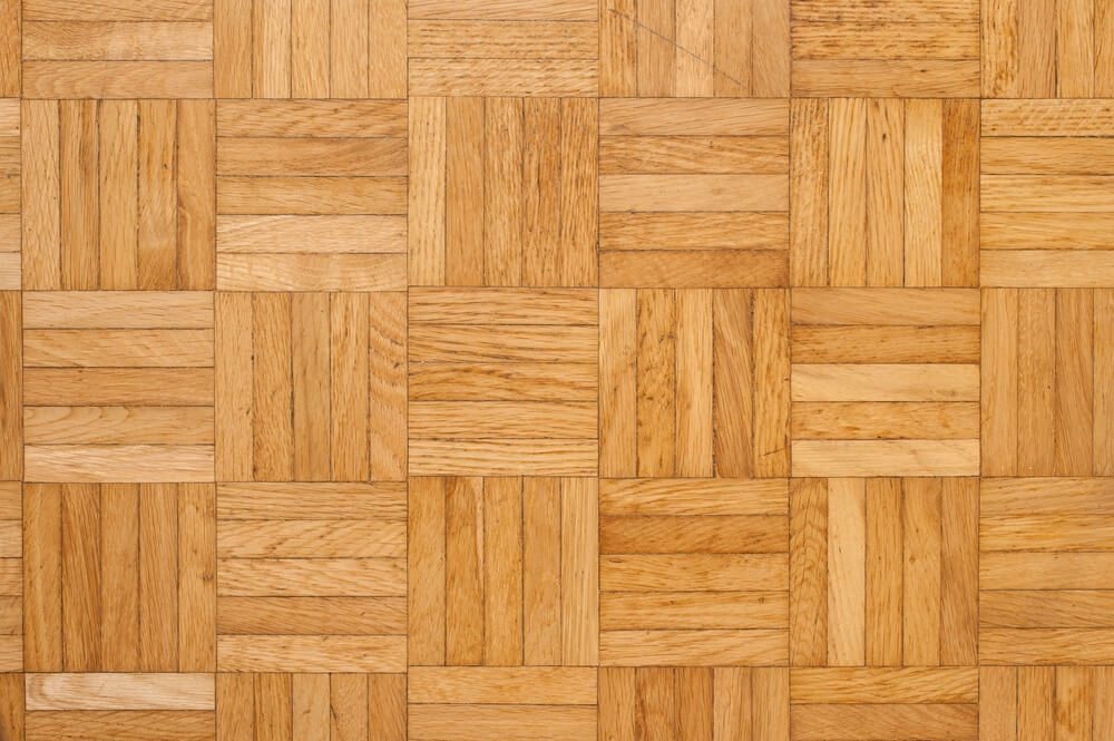 A close-up view of a basketweave-pattern parquet wood floor, featuring alternating rectangular wood blocks arranged in a grid. The floor has a warm, natural wood tone with visible grain patterns, providing a classic and elegant design.