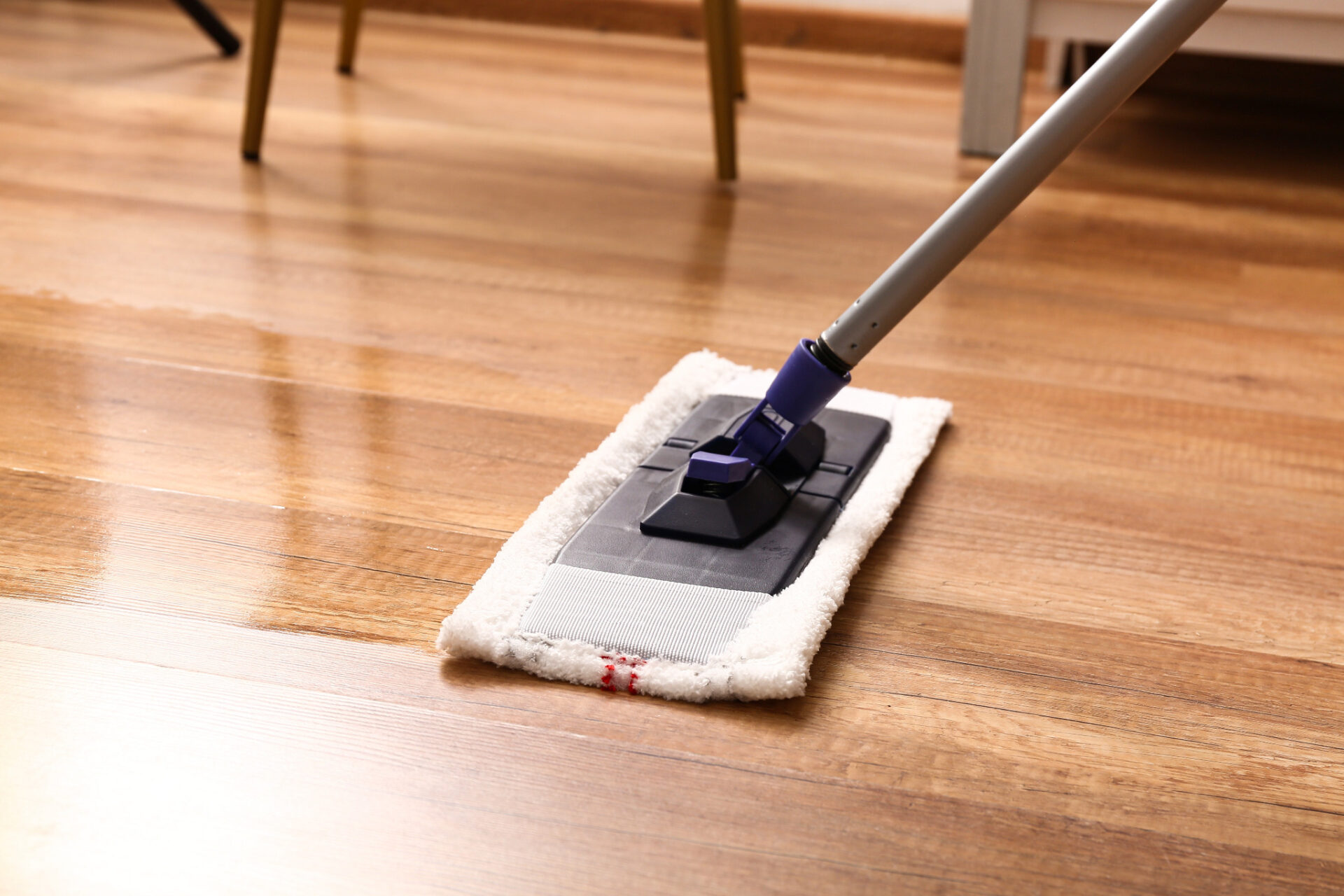 A close-up of a white microfiber flat mop cleaning a light-colored beech hardwood floor, illustrating routine aftercare for sanded floors.