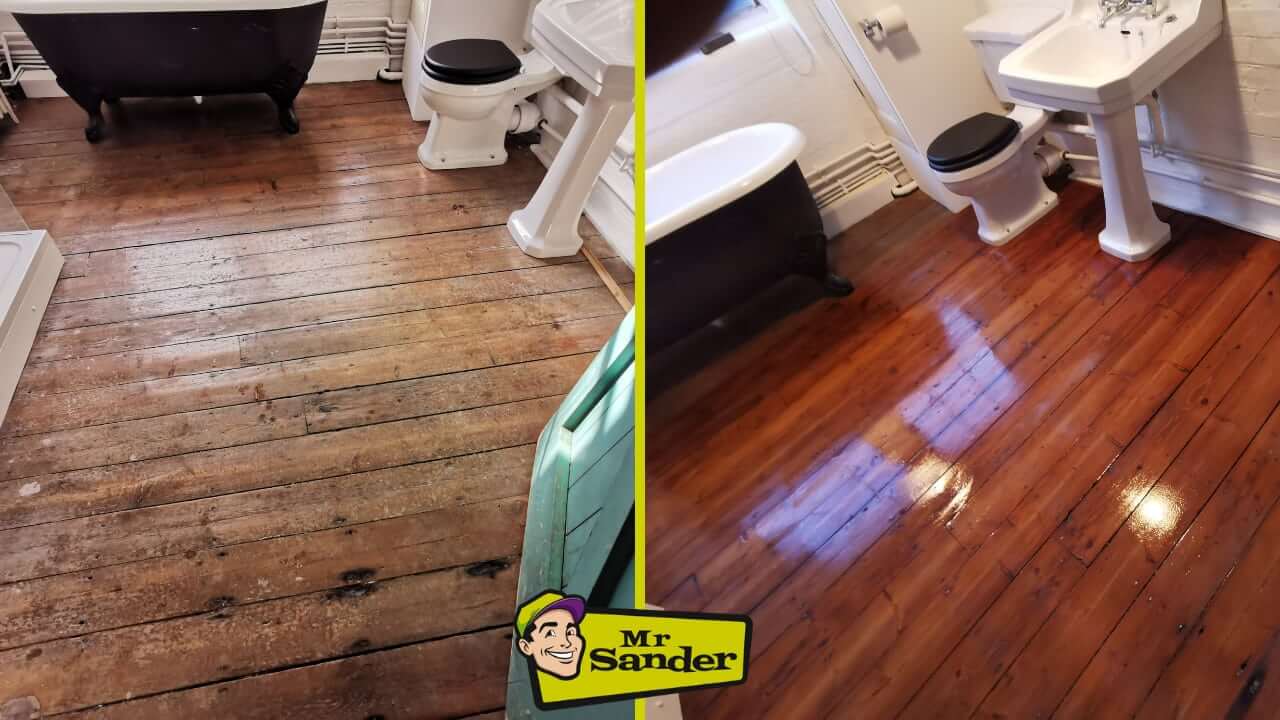 A before-and-after comparison of a bathroom floor in Hutton. The left side shows the floor in its original, worn state with a rough and dull appearance. The right side displays the floor after it has been sanded and refinished, revealing a shiny, dark wood finish. The bathroom fixtures, including a black clawfoot bathtub, a toilet, and a pedestal sink, are consistent in both images. The Mr Sander® logo is visible in the bottom center of the image.