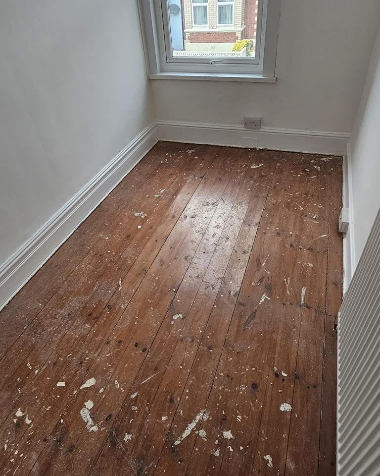 A top-down view of worn and paint-splattered Pine floorboards in a small room before a professional Floor Sanding Service.
