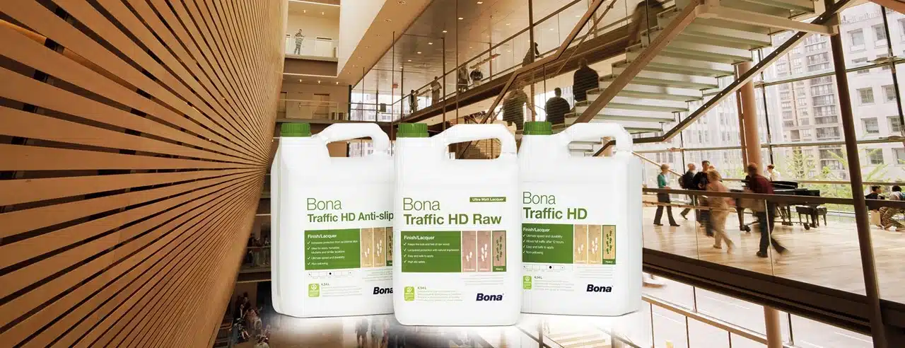  Three bottles of Bona Traffic HD floor finish products displayed in the foreground, with a spacious and modern indoor setting in the background.