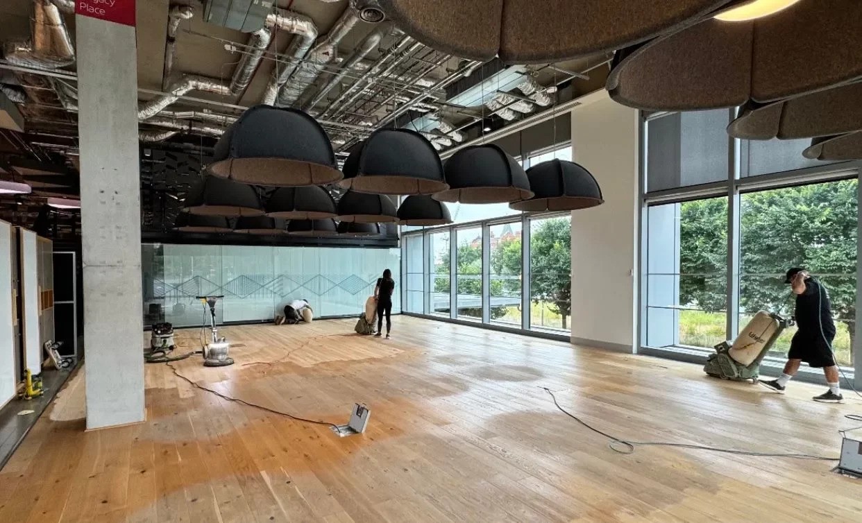 Professional floor sanders working on wide plank engineered oak in a large office space to assist in bringing life back to dark, scuffed surfaces.